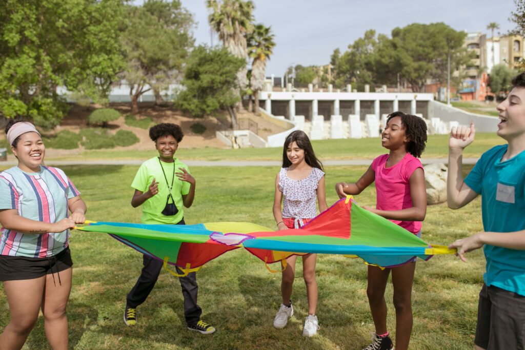 A group of youth with varying skin tones plays with a  large parachute outside.