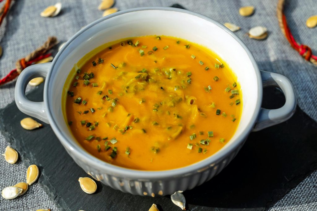 A red/orange soup in a white crock.