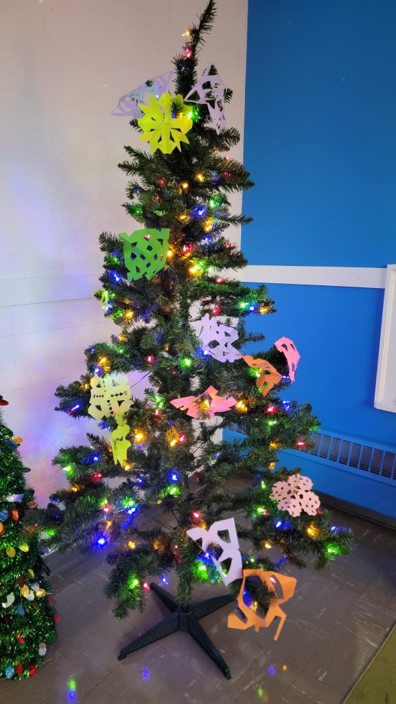 A fake Christmas tree with multicolored lights is decorated with colorful paper snowflakes.